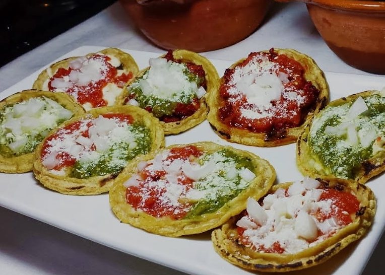 A platter of picaditas topped with red and green salsa, white onion and crumbled cheese.