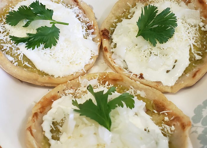 Three picaditas topped with green salsa, crema, cheese and fresh cilantro.