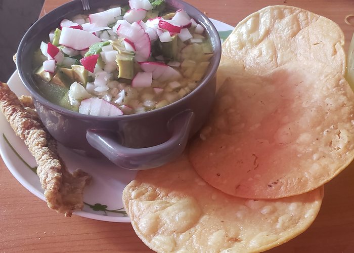 A bowl of pozole with radish and onion, served with tostadas and chicharron.