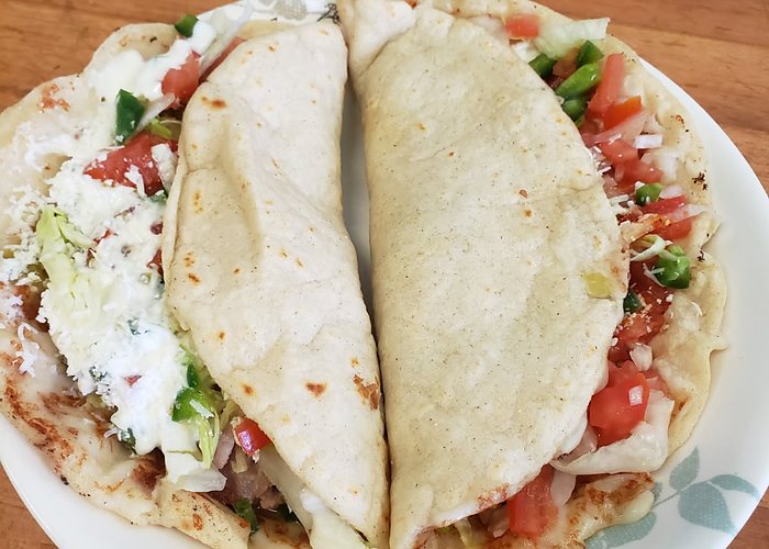Two corn tortilla quesadillas on a plate with lettuce, tomato and crema.
