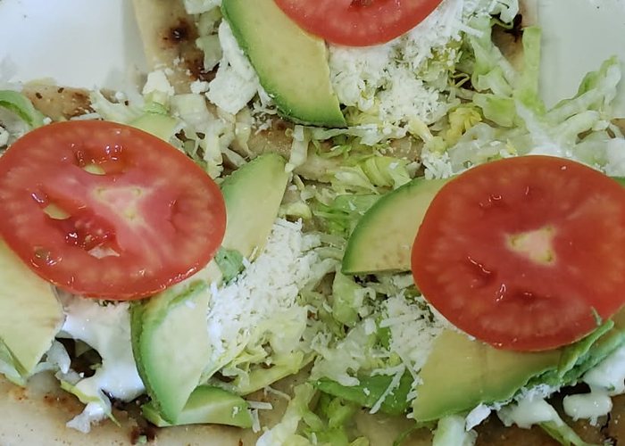 Sopes topped with shredded lettuce, avocado, sliced tomato, crema and cheese.