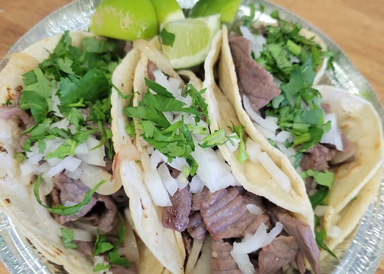 Steak tacos on soft corn tortillas with white onion, fresh cilantro and lime wedges.